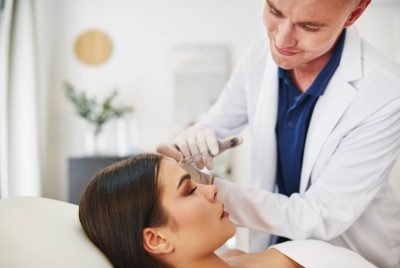 Smiling male doctor performing a botox injection to the forehead of a woman lying on a table in a beauty clinic